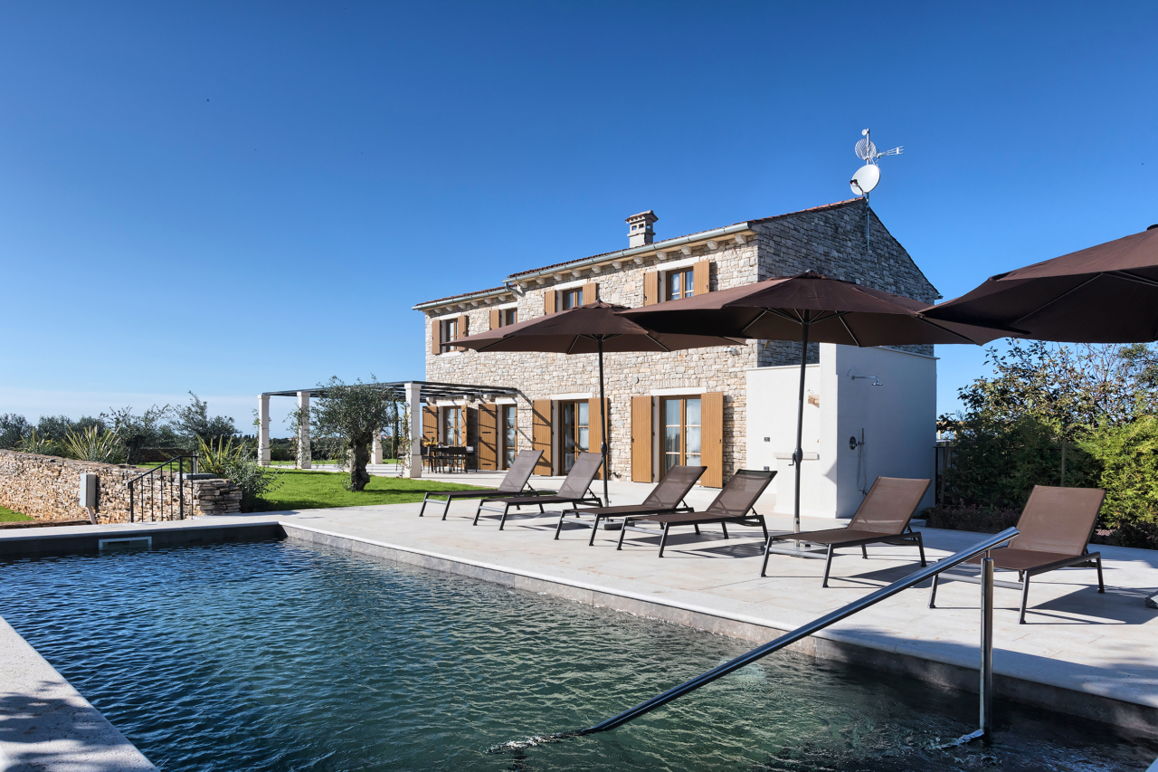 A stone villa with heated swimming pool and outdoor terrace with sunbeds and umbrellas.