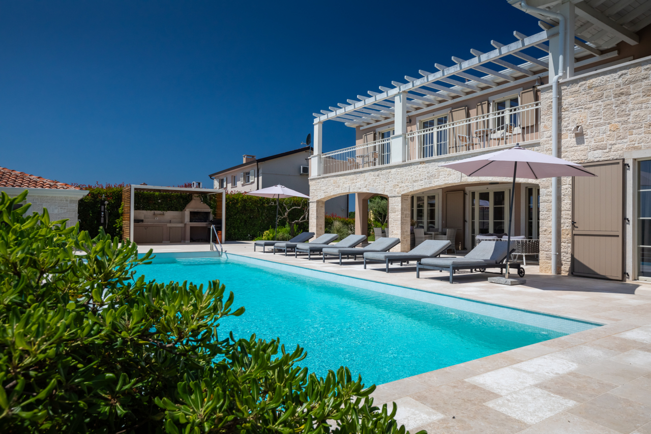 Lussuosa villa in pietra con piscina e terrazza esterna con lettini, ombrelloni e barbecue coperto.