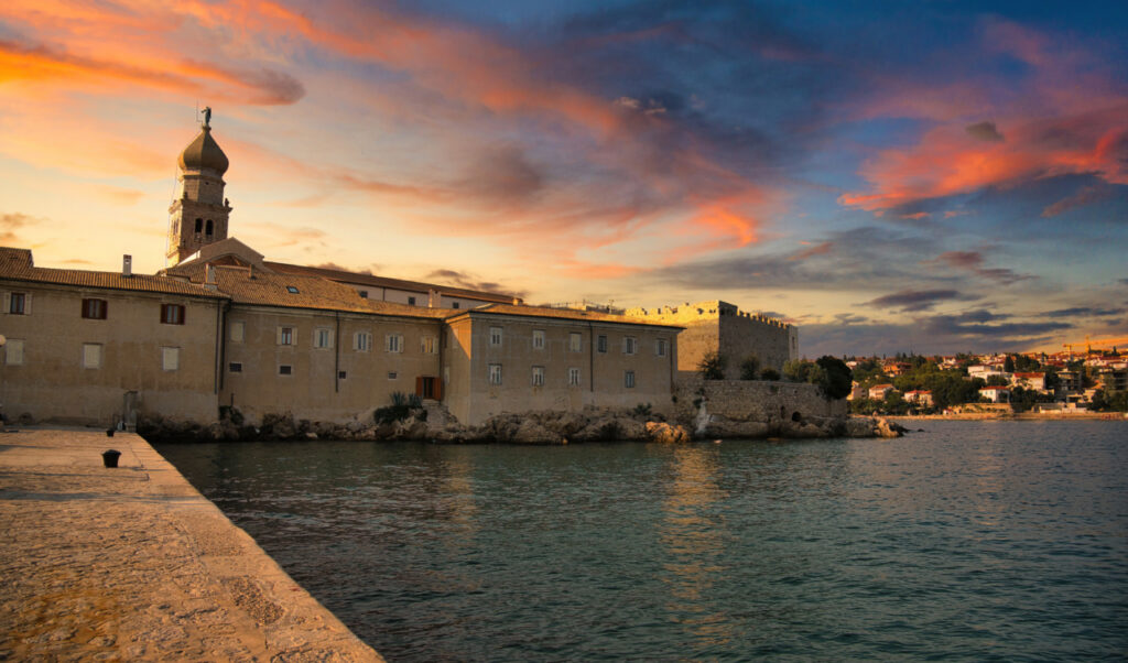 Un castello medievale sul mare, fotografato al tramonto dal bastione di pietra sulla sinistra.