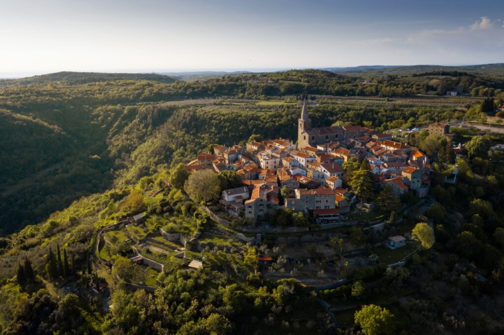 Una vista a volo d'uccello di un'idilliaca città medievale su una collina circondata da altre verdi colline.