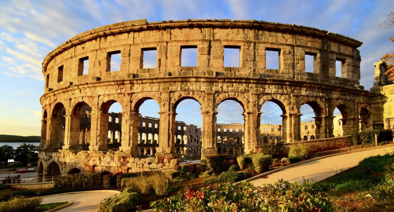 Roman amphitheater in Pula during golden hour with garden and path in front.