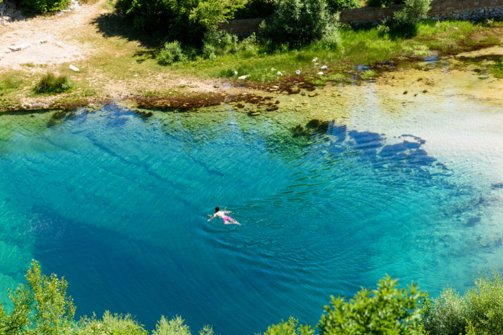 Die Quelle des Flusses Cetina in Form eines Sees mit klarem türkisfarbenem Wasser; die Quelle ist von Vegetation umgeben und in der Mitte befindet sich ein Schwimmer.