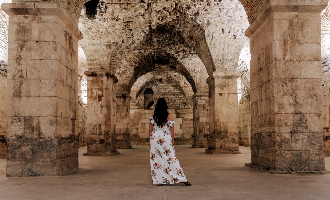 A woman photographed from behind in the middle of the spacious stone cellar of a Roman palace