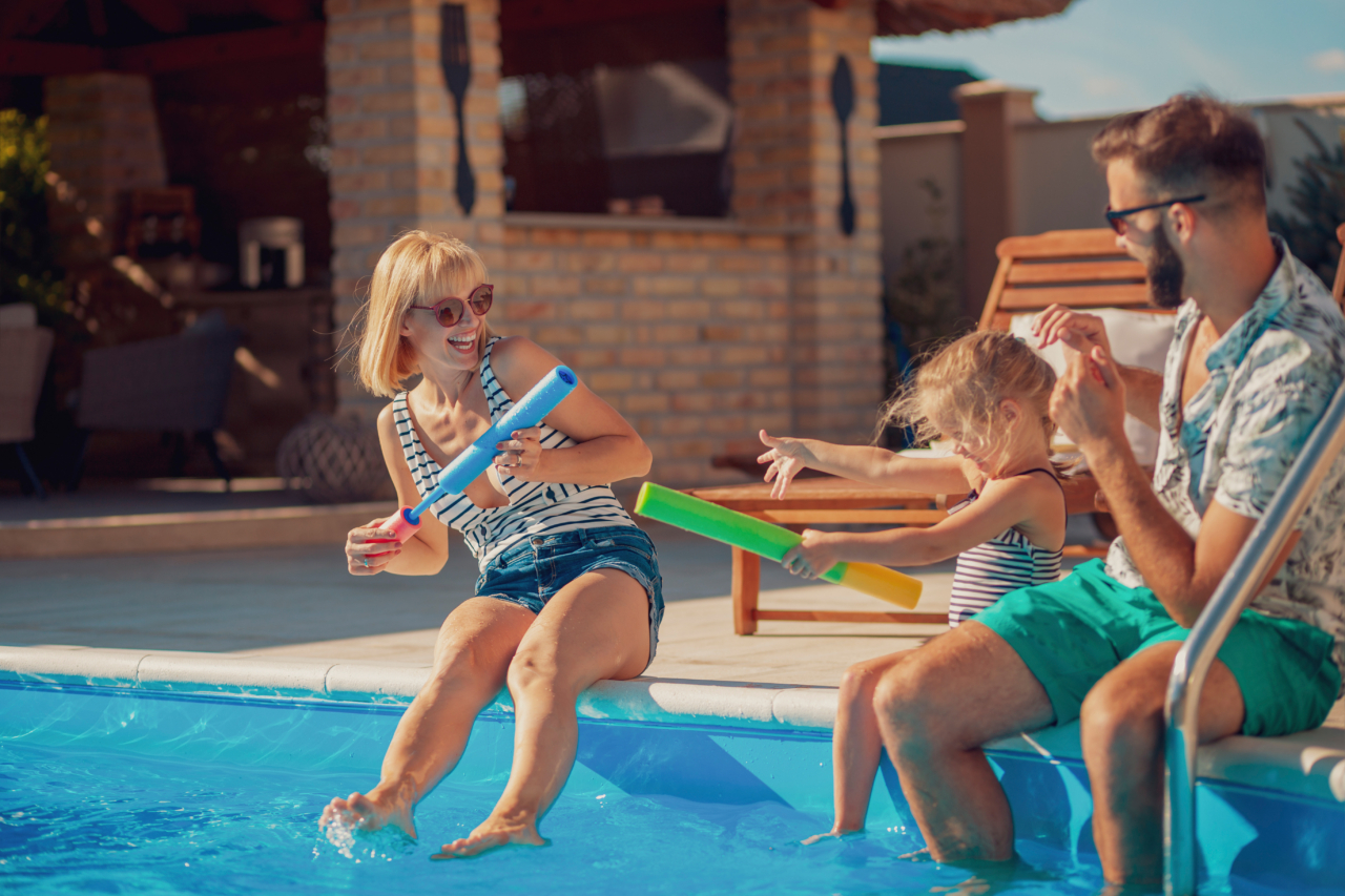 Junge Eltern haben Spaß beim Spielen mit ihrer Tochter am Swimmingpool und bespritzen sich gegenseitig mit Wasser